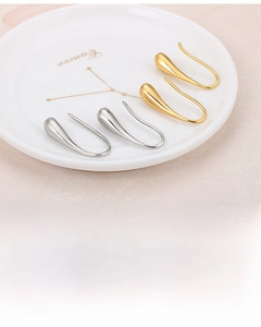 Detail of gold and silver teardrop earrings on a white ceramic tray with polished finish