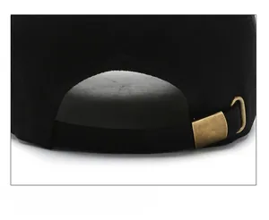 Close-up of black cotton baseball cap showing adjustable bronze metal buckle and fabric texture
