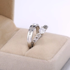 Detail of silver couple rings with cross and heart designs in a beige jewelry box