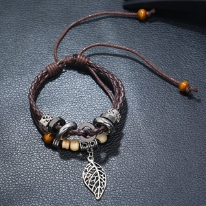 Detail of multilayer leather bracelet with silver leaf charm and wood beads on black background
