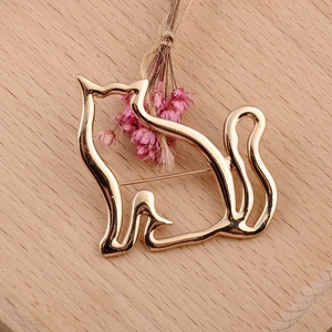 Detail of a minimalist gold hollow cat brooch on a natural wooden background with dried flowers