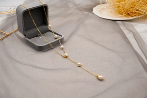 Close-up of golden Y-shaped sweater necklace with freshwater pearls on a velvet box