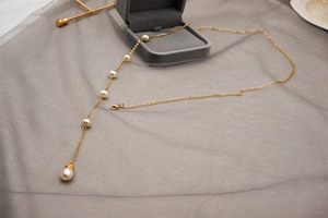 Detail of adjustable gold titanium Y-necklace with freshwater pearls on mesh background