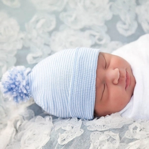 Close-up of a blue and white striped knit baby hat with a soft decorative pom-pom