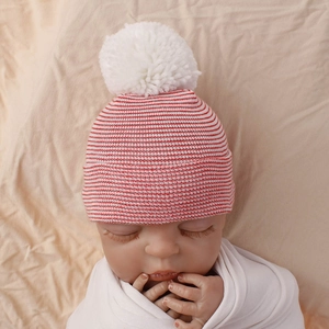 Detail of red and white striped knit baby hat with soft plush pompom for newborns