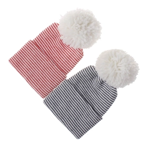 Detail of two striped newborn beanies with large white pom-poms in red and navy