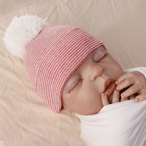 Close-up of red and white striped newborn knitted hat with a cute white pompom detail