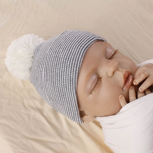 Close-up of blue and white striped newborn knit hat with a soft white plush pom-pom detail