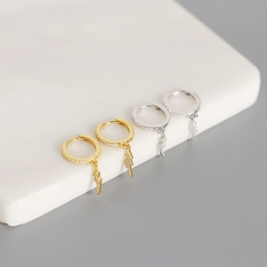 Macro detail of gold and silver huggie hoop earrings with zircon lightning pendants