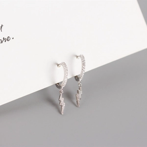 Macro shot of silver hoop earrings featuring lightning bolt charms with zircon inlay detail