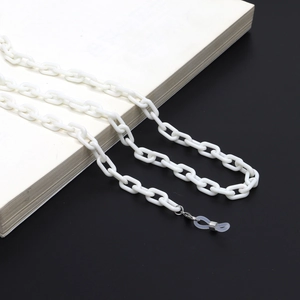 Close-up of a white acrylic glasses chain with silver clips on a white book surface