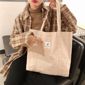 Detail showing beige canvas tote bag with reinforced handles and decorative text patch