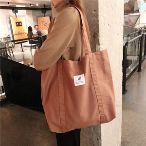 Detail of solid color canvas tote bag with shoulder straps and decorative woven label