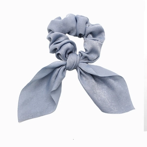 Detail of dusty blue bow hair scrunchie with silky fabric texture on white background
