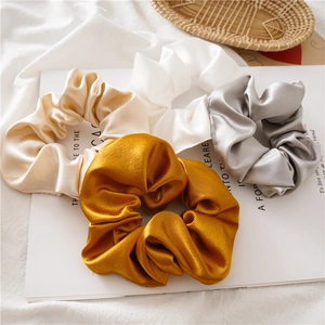 Detail of four satin scrunchies in gold, white, yellow, and grey on a magazine