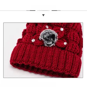 Détail du bonnet rouge en maille avec décoration florale et accents en strass