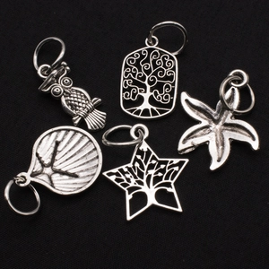 Macro shot of silver owl, starfish, and shell charms with open rings on black background