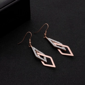 Boucles d'oreilles géométriques en or rose avec cristaux sur fond texturé noir