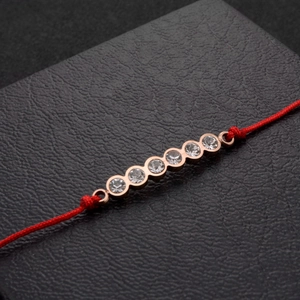 Dettaglio macro del bracciale con cordino rosso e sette zirconi incastonati in oro rosa