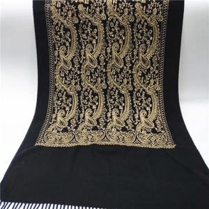 Close-up of golden paisley embroidery and fringe on black cashmere-style scarf
