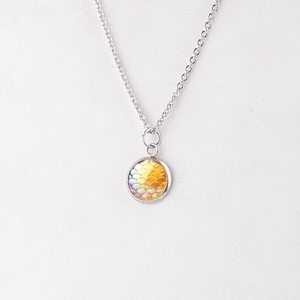 Close-up of circular pendant with orange fish scale pattern on stainless steel chain