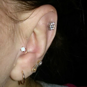 Vista macro de pendientes de flor, opalo y corazon en oreja con acabado dorado