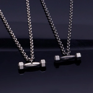 Colliers avec pendentif haltère en acier titane poli sur fond noir réfléchissant