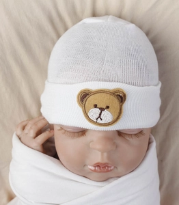 Close-up of white newborn knit hat with cartoon bear embroidery on soft ribbed cotton