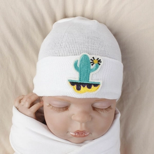 Detail of white newborn knit hat featuring a green cactus embroidery on soft cotton fabric