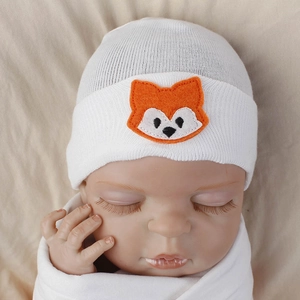 Close-up of white knit baby beanie with cute orange fox embroidery on soft fabric