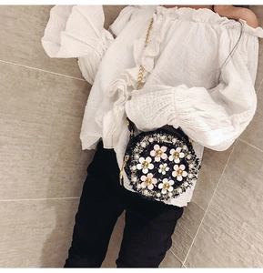 Girl's black woven round shoulder bag with floral and pearl accents worn with gold chain