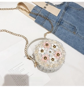 Detail of a round cream woven mini bag with 3D floral accents and golden chain