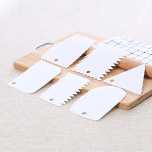 Detailed set of white plastic cake scrapers with varied edges on a wooden board