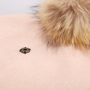 Detailed close-up of a pink wool knitted beret with a fluffy natural fur pompom and metal stud