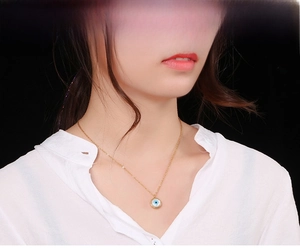 Close-up of golden Evil Eye necklace with blue pendant on a model wearing white shirt