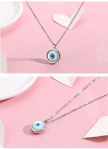 Macro shot of silver evil eye necklace pendant with blue resin inlay on a pink backdrop