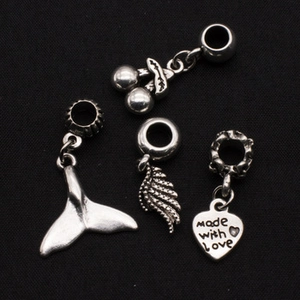 Macro shot of silver cherry, whale tail, wing and heart pendants on black surface