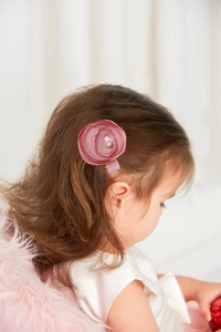Detailed view of a pink ribbon flower hair clip with a pearl center worn by a child