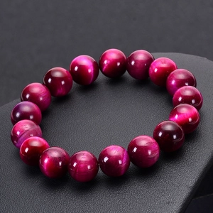 Close-up of polished rose red tiger eye stone beads with chatoyancy on black display