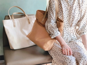 Detail of canvas tote bag featuring brown PU leather handles and metal rivet reinforcement