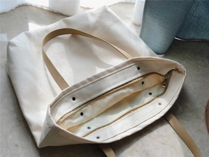 Detail of off-white canvas tote bag with metal zipper and snap button closure
