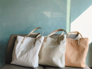 Three canvas tote bags in white, cream, and apricot colors on a grey leather sofa
