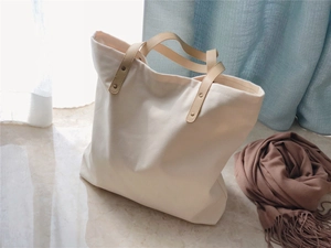 Detail of white canvas tote bag featuring beige leather handles and metal rivet fasteners