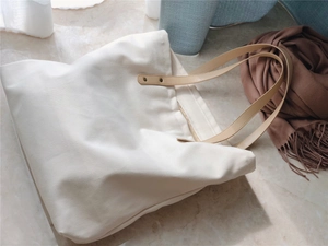 Detail of off-white canvas tote bag featuring premium brown faux leather handles