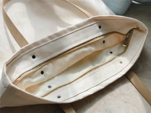 Top view of cream canvas tote bag showing faux leather handles and metal zipper detail