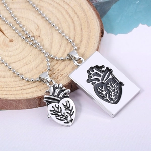 Macro detail of silver anatomical heart pendants for couples displayed on a rustic wood slice
