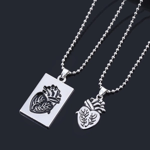 Detailed view of anatomical heart couple pendants with silver ball chains on gray base