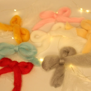 Flat lay of colorful macaron wool felt bows on plush white background with fairy lights