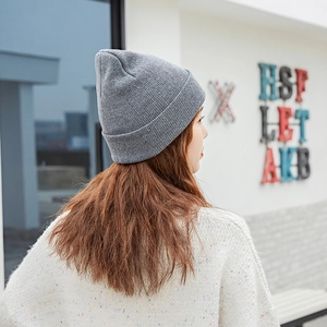Back view of a model wearing a grey knitted beanie hat in a natural outdoor setting