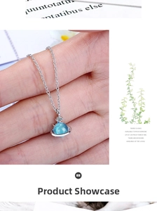Detail of blue planet pendant necklace held by hand featuring a translucent bead